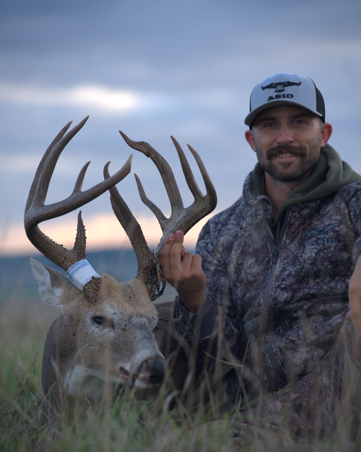 Kaleb Greiner kneeling behind a mature public-land whitetail buck he took in North Dakota