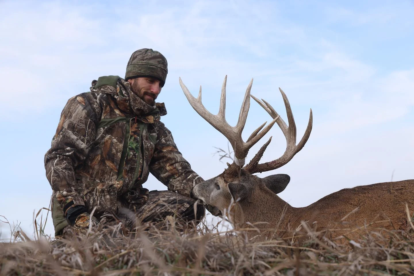 Kaleb Greiner kneeling beside a mature Iowa whitetail buck